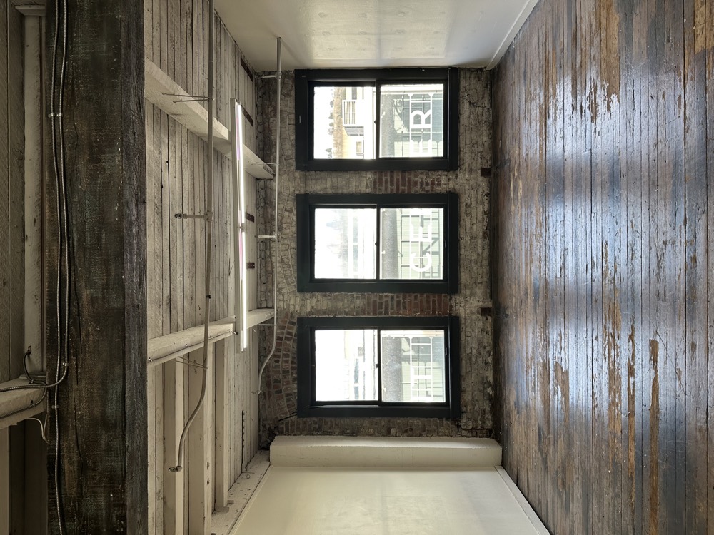 The empty room with three tall windows and original plank floors