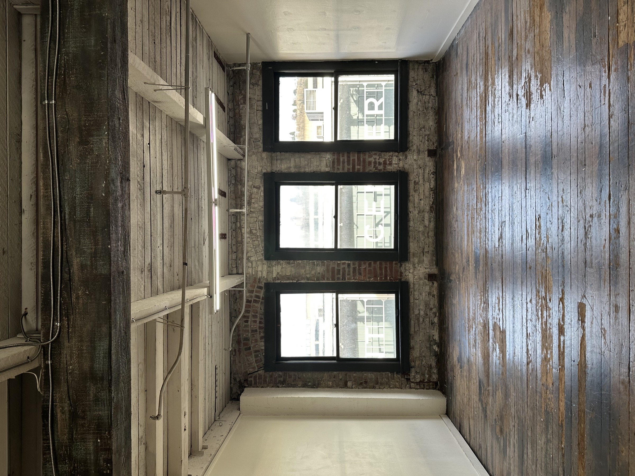The empty room with three tall windows and original plank floors